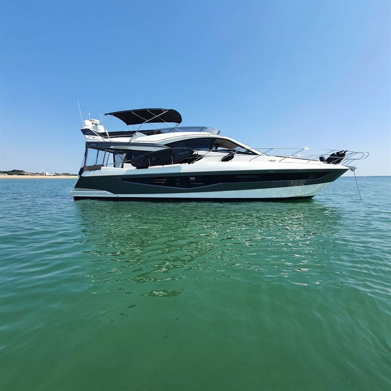 Luxury motor yacht anchored on clear blue water, with a sunny sky and shoreline visible in the background.